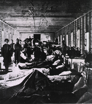 Black and white photograph of the inside of a hospital ward with injured soliders laying on beds.