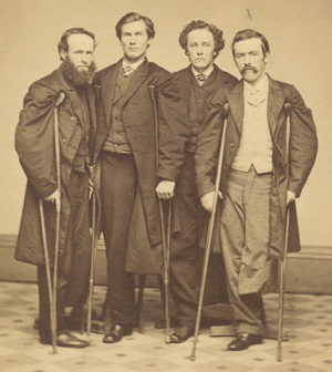 Veterans John J. Long, Walter H. French, E. P. Robinson, and an unidentified companion, 1860s. Courtesy Library of Congress Sepia photograph of four smartly dressed men, each missing a leg and using crutches, standing in a group.