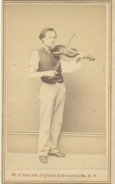 Sepia photograph of a Burritt Stiles, standing wearing pants, a shirt, and a dark vest. He is holding a violin to his chin with his left hand. On his right arm where it was amputated near the shoulder, he is wearing a prosthetic arm and holding a violin bow.
