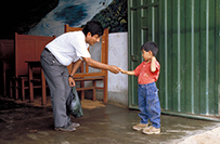 A Latino man leans down to shake the hand of a Latino child.