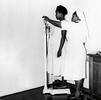 An African nurse weighing a pregnant African patient.