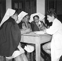 A white doctor and three African nurses sit at a table speaking together.