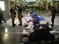Patient lay on gurneys, wrapped in blankets, in an airport hallway as uniformed workers walk by and stand around discussing.
