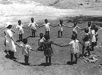 African children play outside, holding hands in a circle while a child stands in the middle.