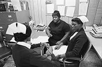 Three African American nurses sit discussing in an office space.