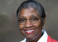 A woman’s portrait wearing glasses and a red jacket with a white shirt.