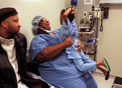 Two people sit while one in scrubs holds up a child.