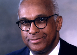 A man’s portrait wearing glasses and a suit and tie.