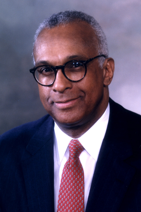 A man’s portrait wearing glasses and a suit and tie.