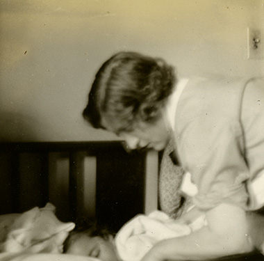 A uniformed, White, female nurse tending to a child in a crib.