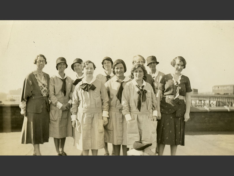 10 White females, 8 in nurse uniforms with cuffs and collars, neck ties, and 2 in dress suits.