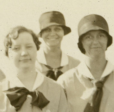 8 White female nurses in uniforms with neck ties, standing in a group.