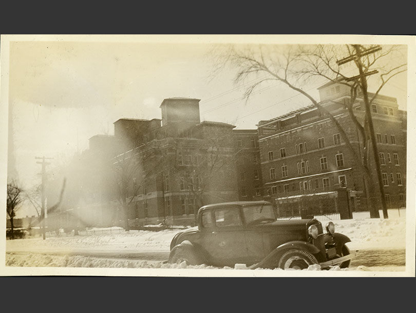 Five-story brick hospital with a Ford Model A parked along snowy road in the foreground.