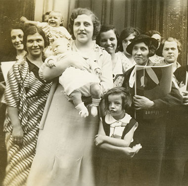 Fourteen women posing as a group, one holding a baby and one with a child in front.