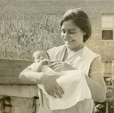 Smiling white woman holding newborn baby outside.