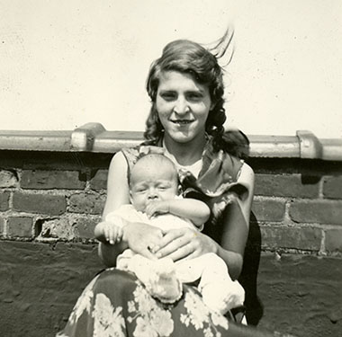 Female sitting on the roof of a building with a baby on her lap.