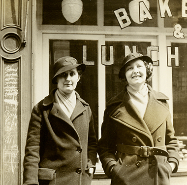 Two White, female nursing students standing outside a storefront in winter coats and cloche hats.
