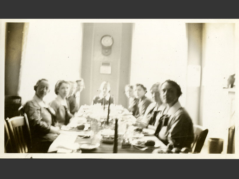 Eight nurses in matching uniforms sitting at a long table for a meal.