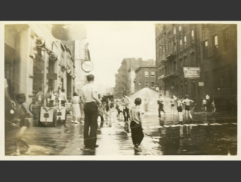 Children playing on a lower Manhattan street under an opened water sprinkle.
