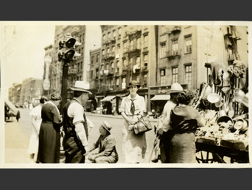 White, female nurse in uniform next to a street peddler's cart on Houston Street, Lower Manhattan.