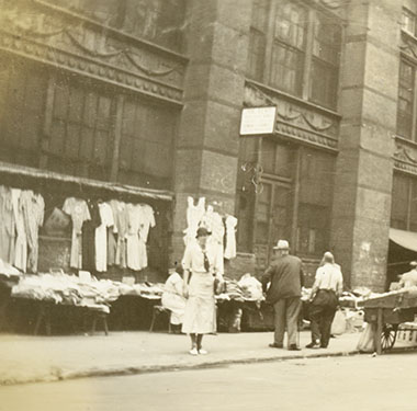 White, female nurse standing near several pushcarts on a street in Lower Manhattan.