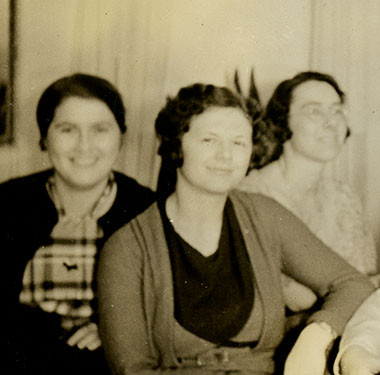 6 women smiling and sitting closely together in a living room.