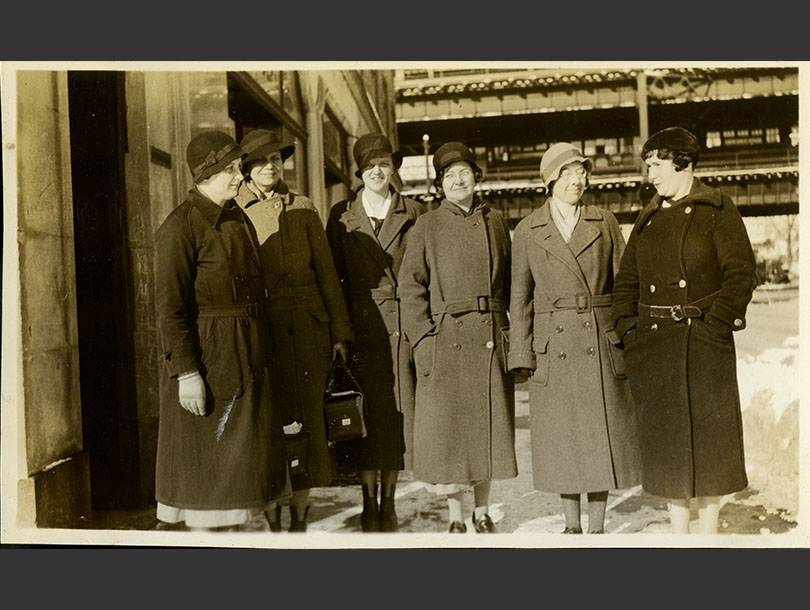 Six White female nurses in overcoats and cloche hats, Gun Hill elevated rail line in background.