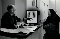 Uniformed white man pointing to an x-ray of a chest next to an elderly white woman in a headscarf.