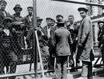 Ten men standing behind a chain-link fence with two uniformed men on the opposite side.