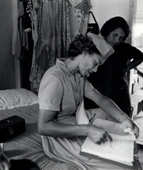 White female nurse in uniform consulting a notebook while in a patient’s home.