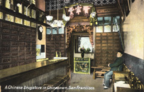 Interior view of shop with tall drawers, chandelier, Chinese writing and vase. Chinese-American man sitting in chair.