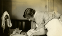 A uniformed, white, female nurse tending to a child in a crib.