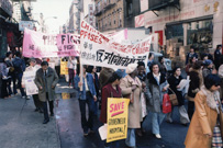 People protesting in the street with banners in English and Chinese.