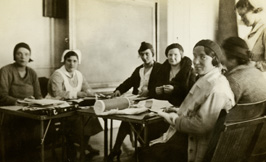 A group of women and nurses sit working around tables.