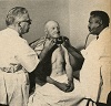 An African American and White man jointly examine a seated patient.