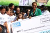 African American woman holds a large check, surrounded by a multiracial group of people.