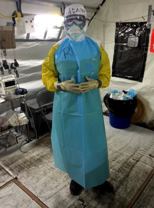 Woman fully covered in scrubs and medical encounter gear stands and looks at the viewer.