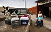 A White woman in a wheelchair is wheeled to a truck by a White woman in white hospital clothing.