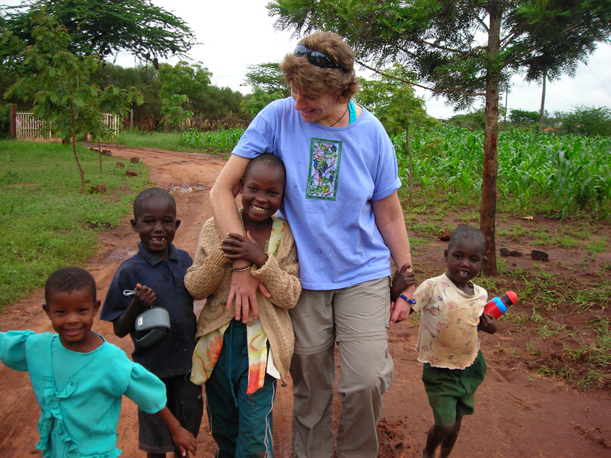 White woman walks with 4 smiling African children.