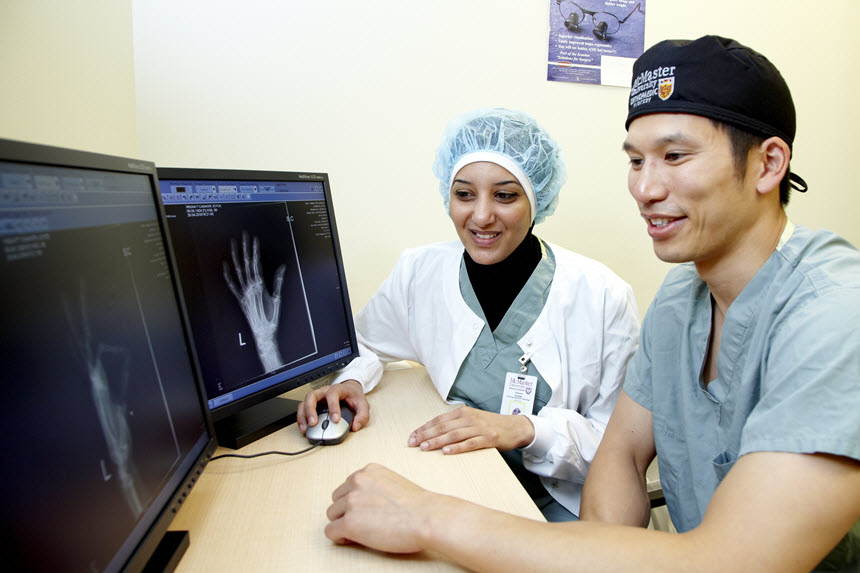 Man and woman in scrubs look at an x ray on a computer screen. 