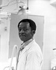 African American man in lab coat looks at viewer with head turned.