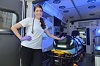 Smiling White woman wearing gloves poses in front of a stretcher in the back of an ambulance.