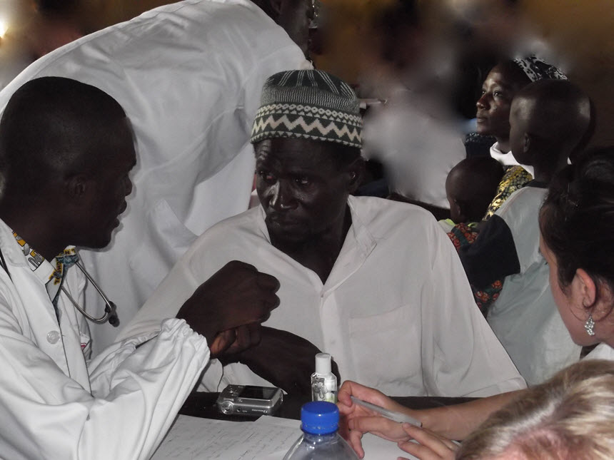 An African man wearing white medical clothing, tents to another African man.