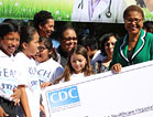 African American woman holds a large check, surrounded by multiracial group of children and teens.