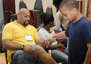 African American boy examines a seated African American man's knee as another boy looks on.