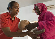 African America woman hands an infant sized mannequin to an African woman.