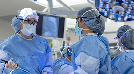 Three people in scrubs perform surgery, one looks off to the right at a screen out of view.