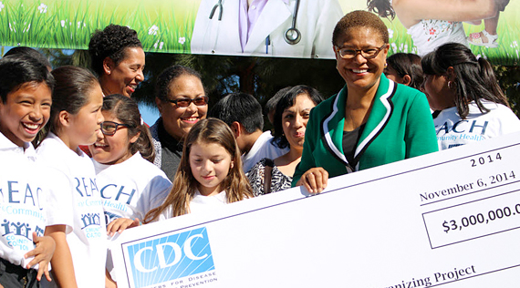 African American woman holds a large check, surrounded by a multiracial group of people.