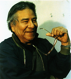 Head and shoulders, right side face view of Jose Perez smiling with his left arm bent at the elbow holding his glasses in his hand.