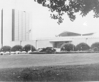 A photograph of the north side view of the National Library of Medicine surrounded by cherry blossom trees and the 10 story Lister Hill center on the left.